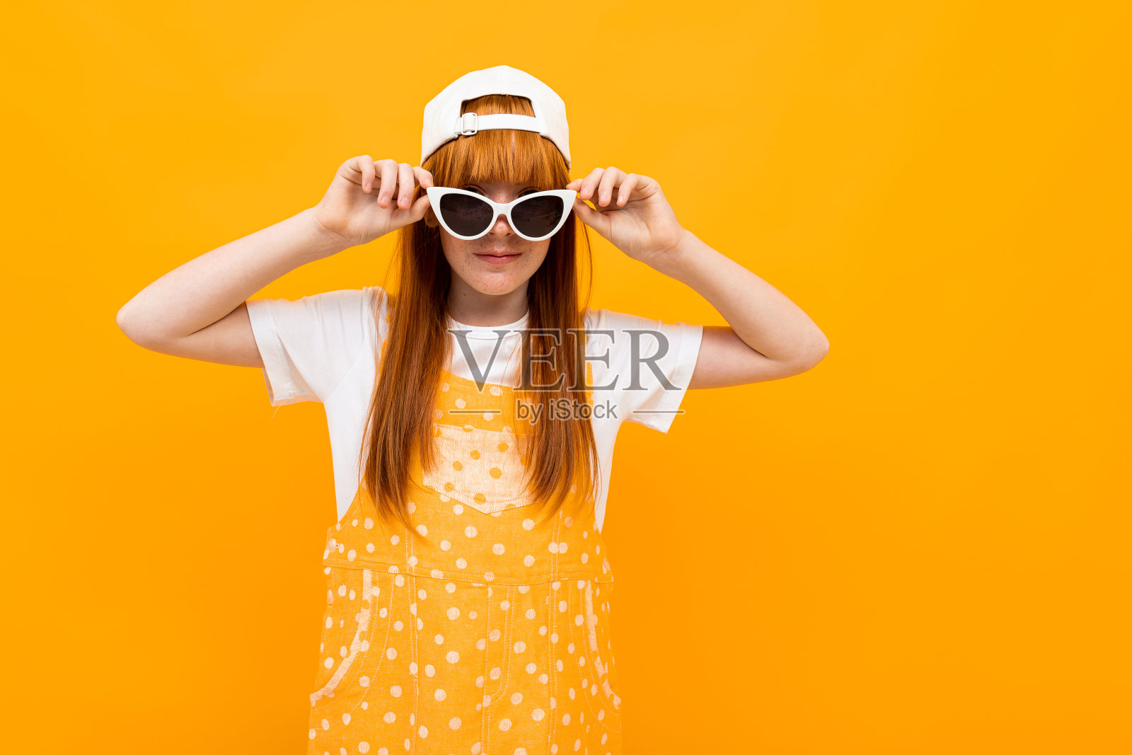 红头发的漂亮女孩在镜头前摆姿势，带着太阳镜在黄色背景上微笑照片摄影图片