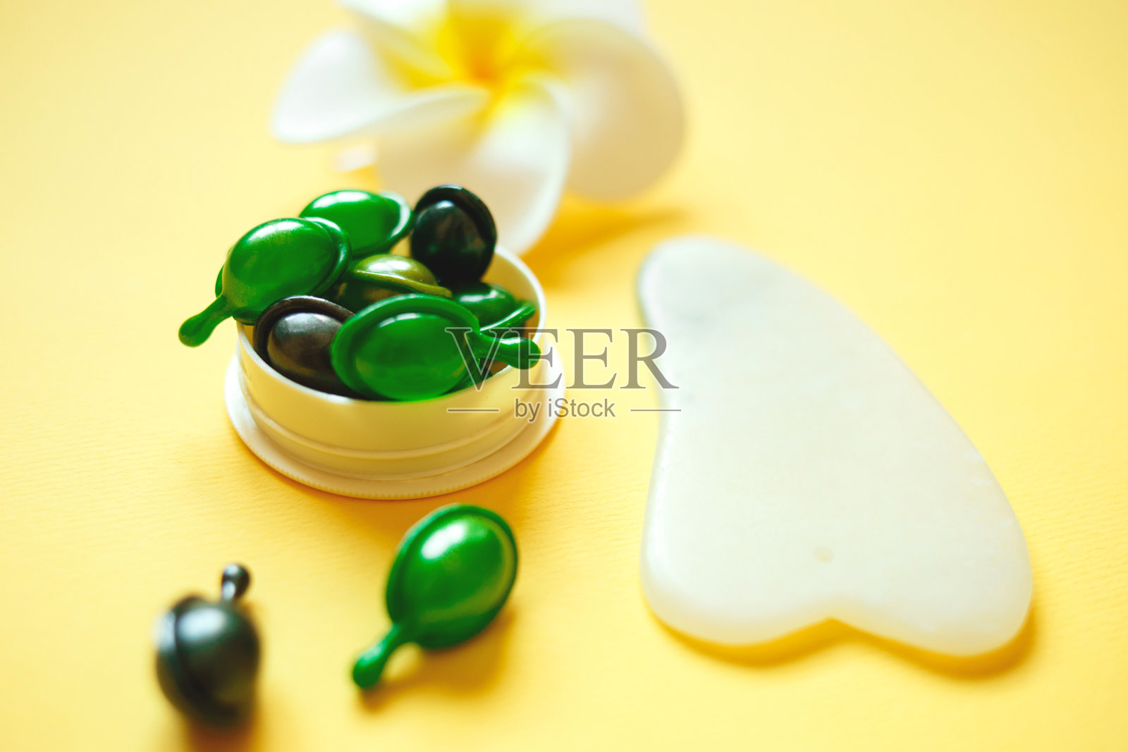 面部按摩工具。刮沙按摩器、精华液、胶囊及花照片摄影图片