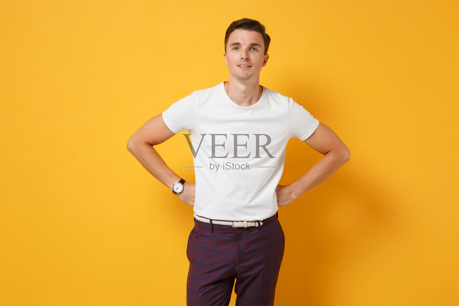 英俊的年轻人男孩20岁在白色t恤摆孤立在黄橙色的背景在工作室。人真诚情感，生活理念。模拟拷贝空间。双手叉腰站着。照片摄影图片