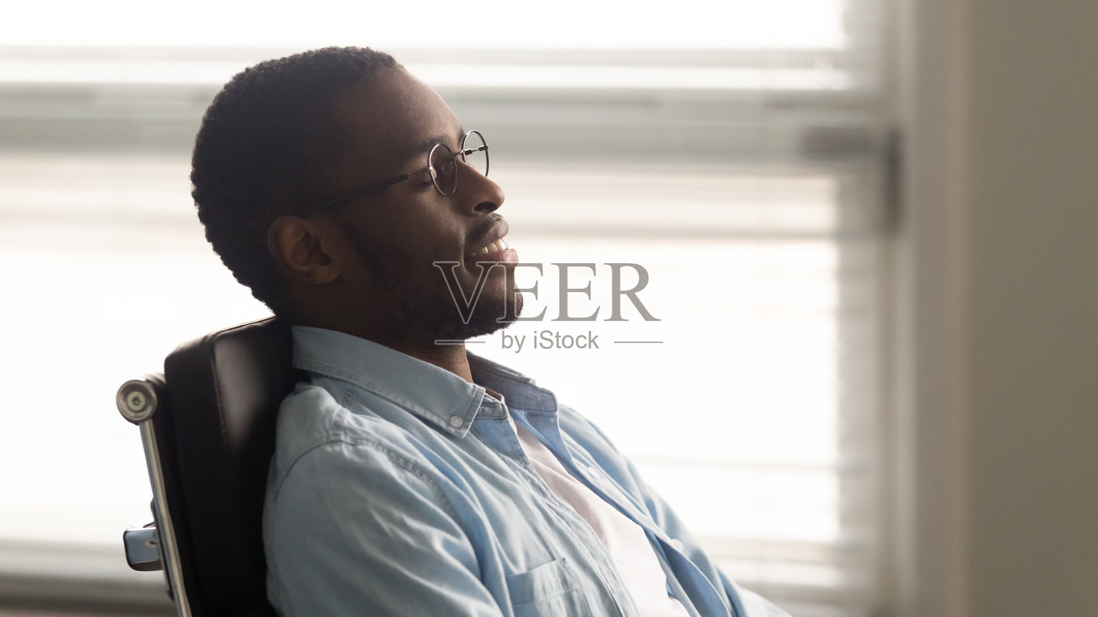 近距离观察非洲裔美国商人在舒适的办公椅上放松。照片摄影图片