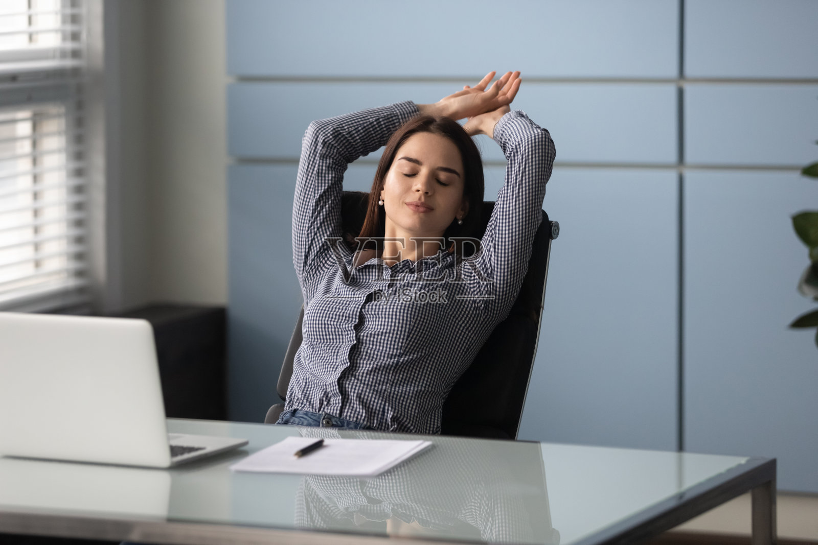 冷静的女商人，双手放在脑后，在舒适的办公室里放松。照片摄影图片