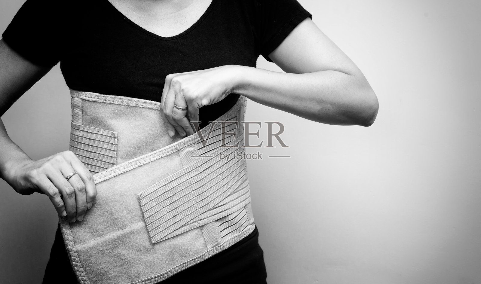 穿着黑色t恤的妇女，穿着背部支撑带，用于背部疼痛和脊柱支撑。黑白色调。医疗护理概念照片摄影图片