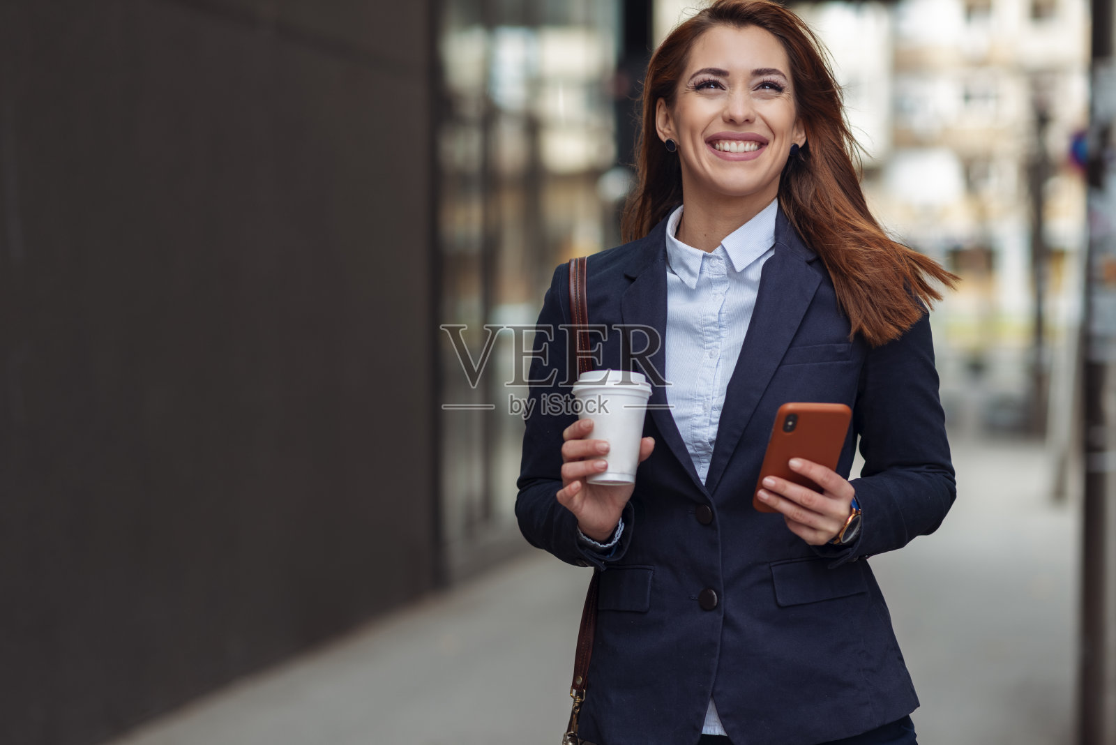 美丽的商务女性在户外散步。拿着咖啡和电话。照片摄影图片
