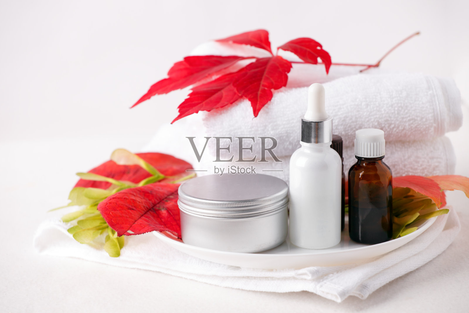 零废弃玻璃化妆瓶及金属瓶，霜、精华、肥皂、油等放在白色的桌子上。秋叶红艳，天然有机美容产品。水疗，皮肤护理，沐浴身体护理。的化妆品照片摄影图片