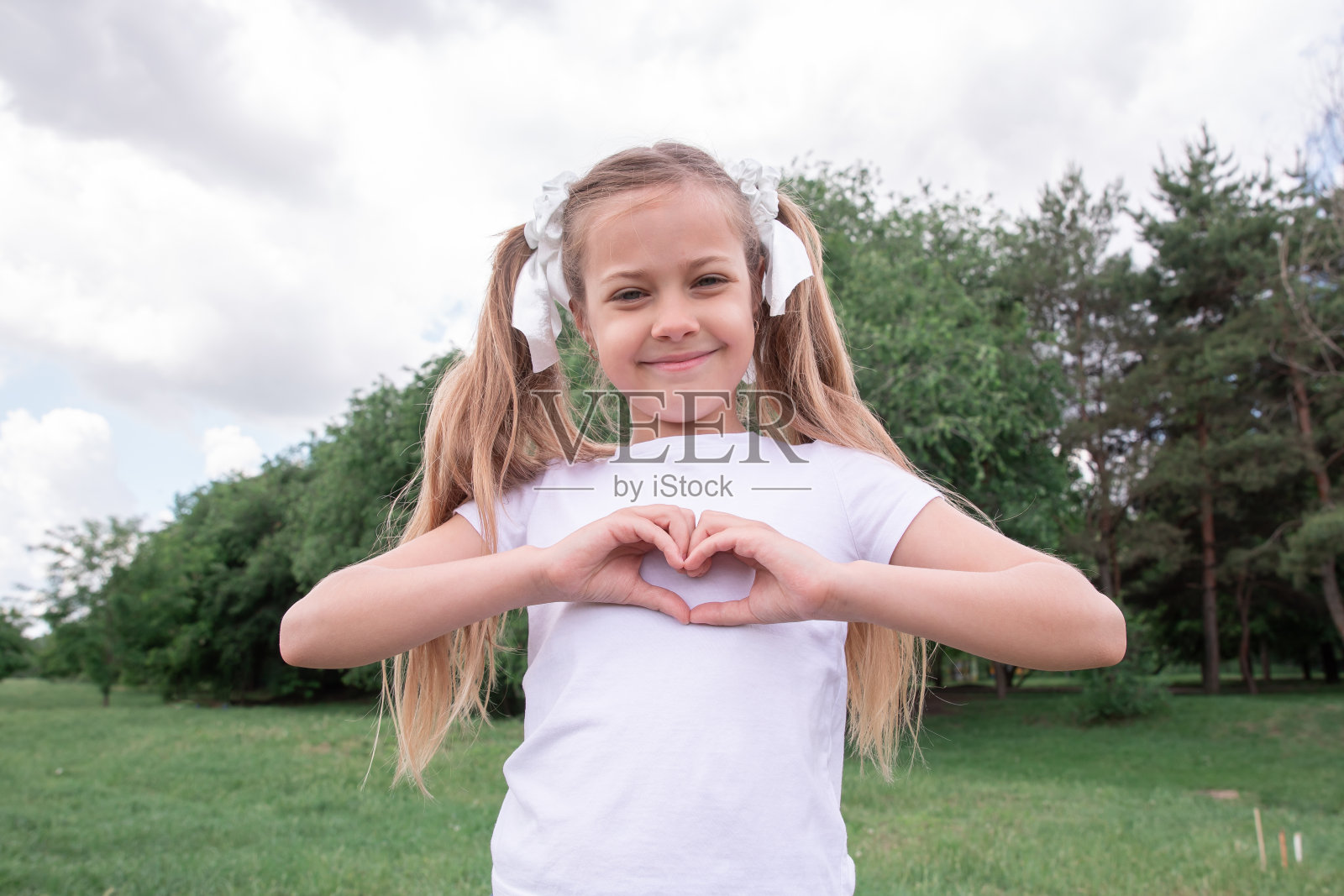 一个小女孩微笑着，用手做了一个心形手势。孩子和爱。照片摄影图片