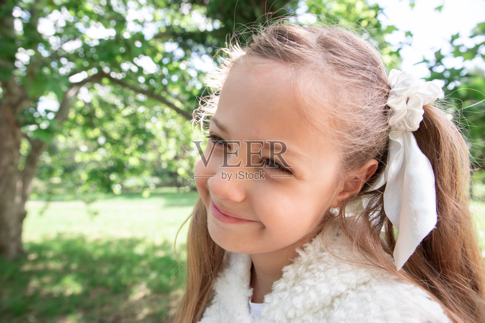 小女孩长着尾巴在绿色的森林里，在公园里。孩子微笑着，拿着一片树叶。照片摄影图片