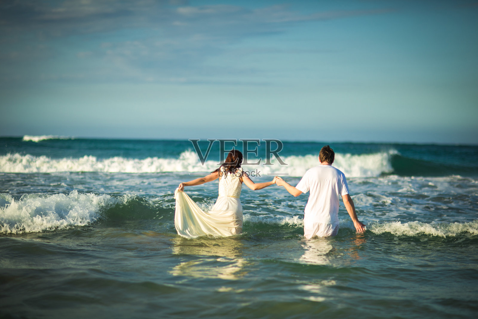 穿着白色衣服的夫妇在海滩的水里。照片摄影图片