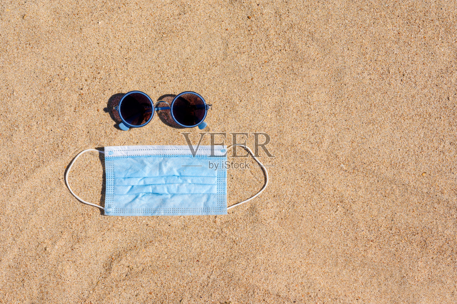 太阳镜和医用口罩躺在沙滩上。照片摄影图片