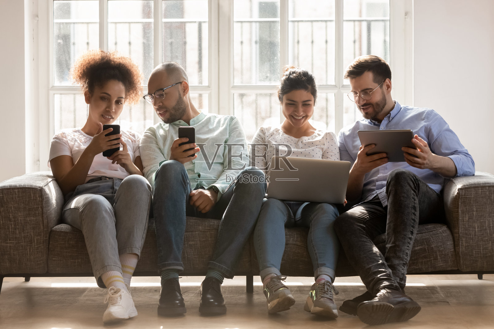 多种族朋友坐在沙发上，用现代电子设备照片摄影图片