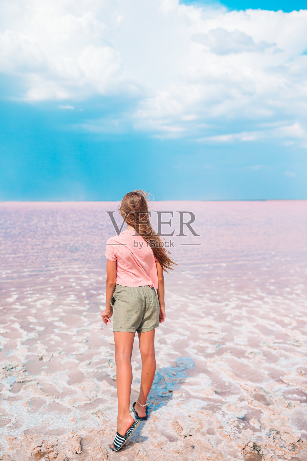 在一个阳光明媚的夏日，女孩在一个粉红色的盐湖上。照片摄影图片