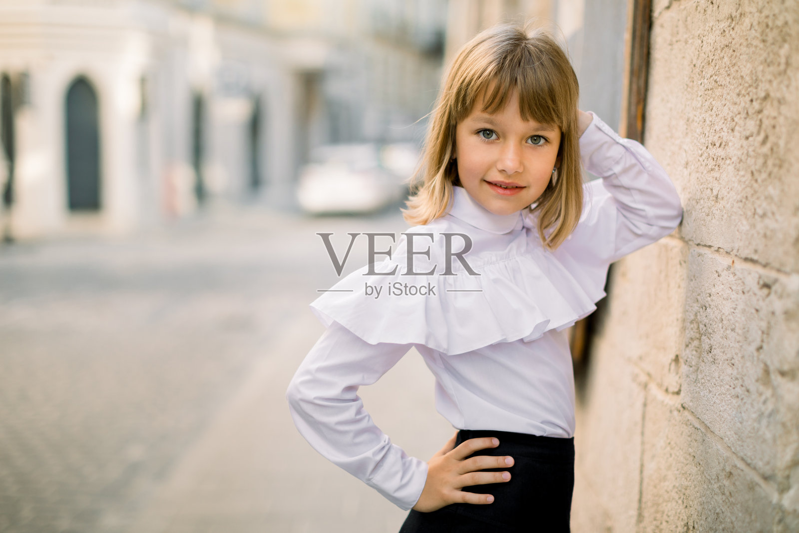 时尚的户外肖像，迷人的小女孩穿着白色衬衫和黑色裙子，倚在美丽的古欧洲城市旧城建筑的墙上。水平拍摄，复制空间照片摄影图片