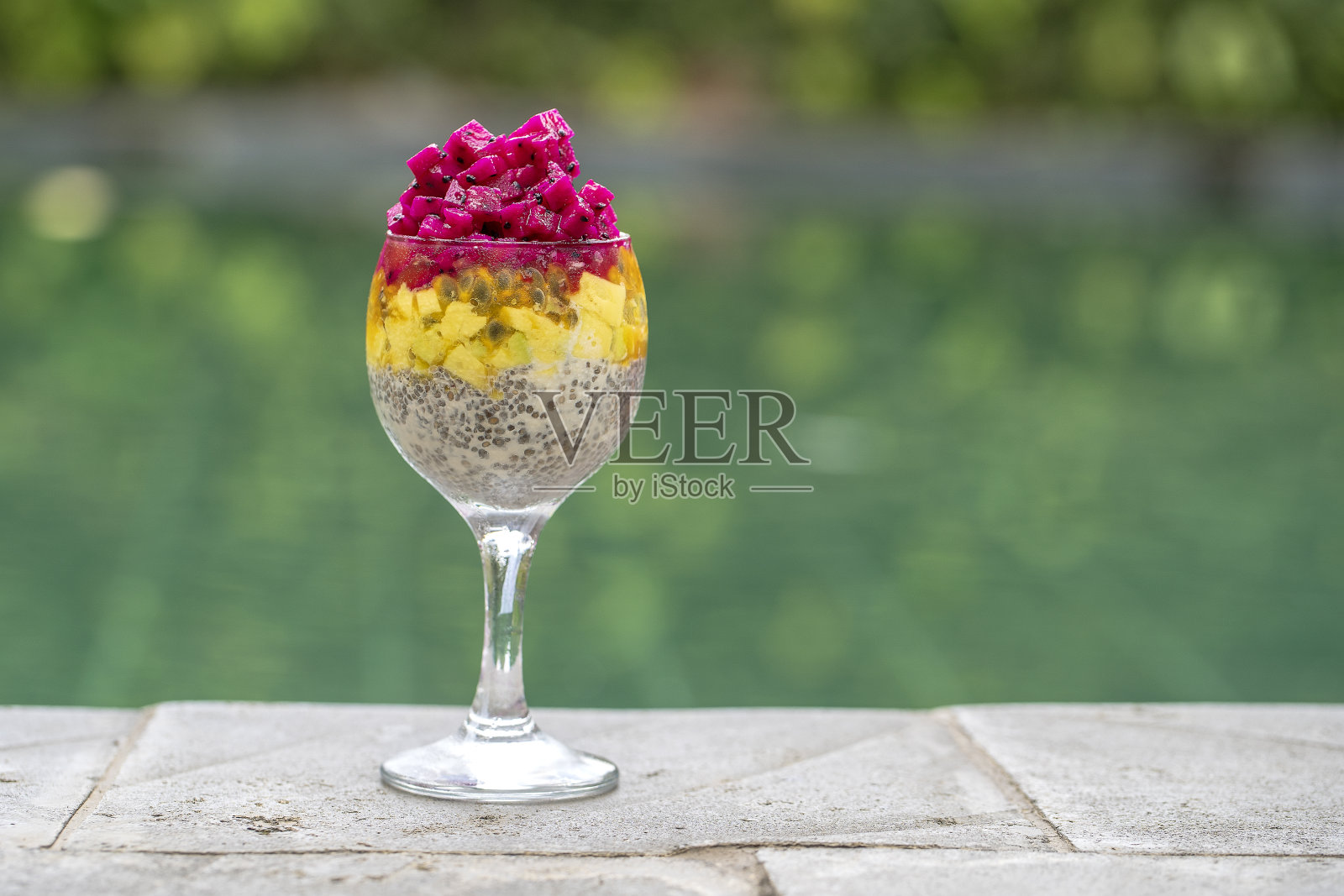 奇亚种子布丁与红色火龙果，百香果，芒果和鳄梨在一个玻璃杯的早餐背景游泳池的水，特写。健康饮食的概念。照片摄影图片