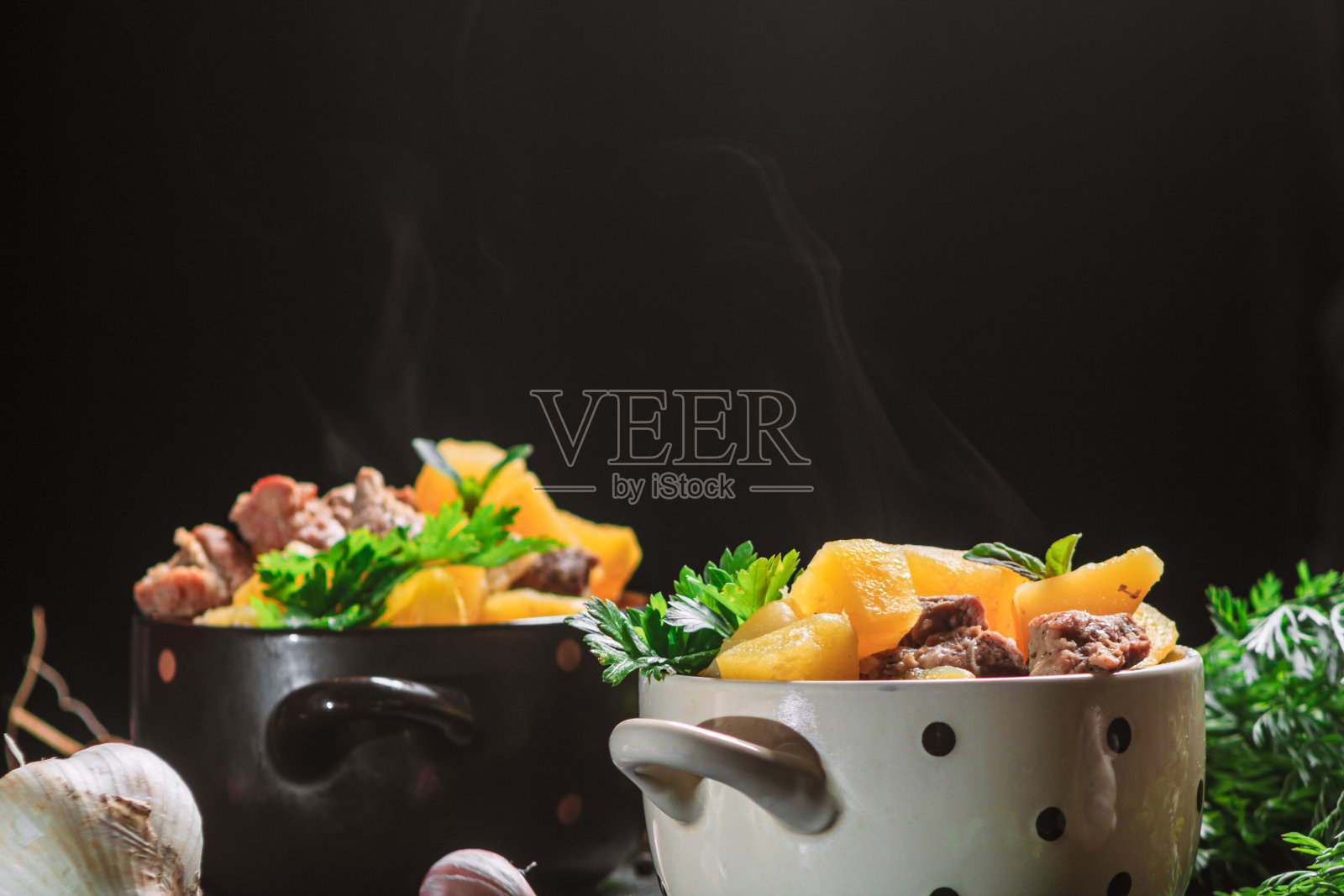 热蒸土豆炖，与肉、猪肉和欧芹一起烤在一个深盘子里，旁边是香料胡萝卜在黑色的桌子上。复制空间，近距离，水平方向照片摄影图片