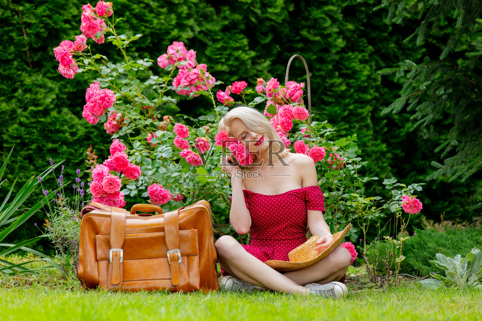 一个漂亮的金发女孩穿着红色的衣服带着手提箱在花园里照片摄影图片