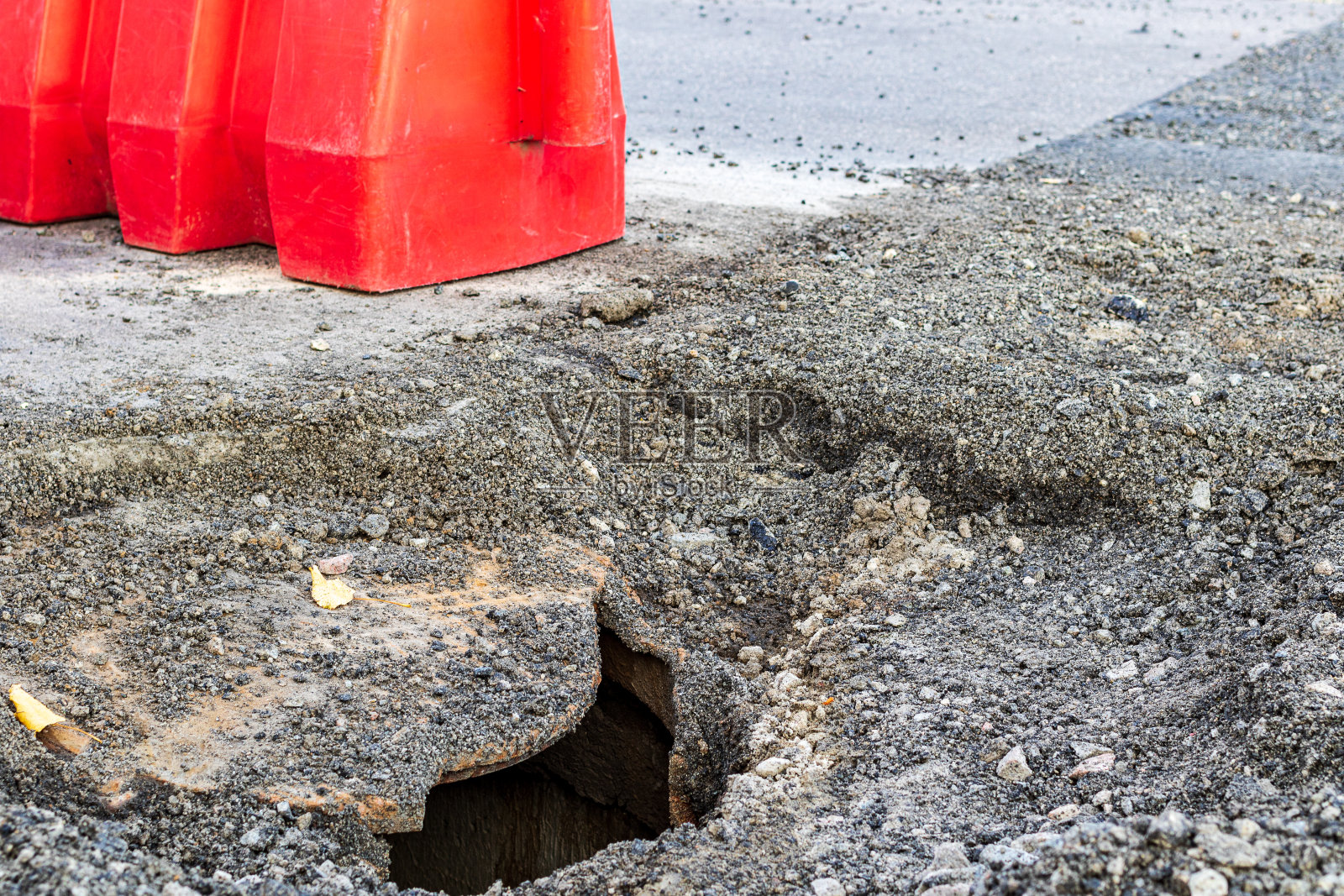 沥青路面上有一个破损的灰铸铁井盖。照片摄影图片