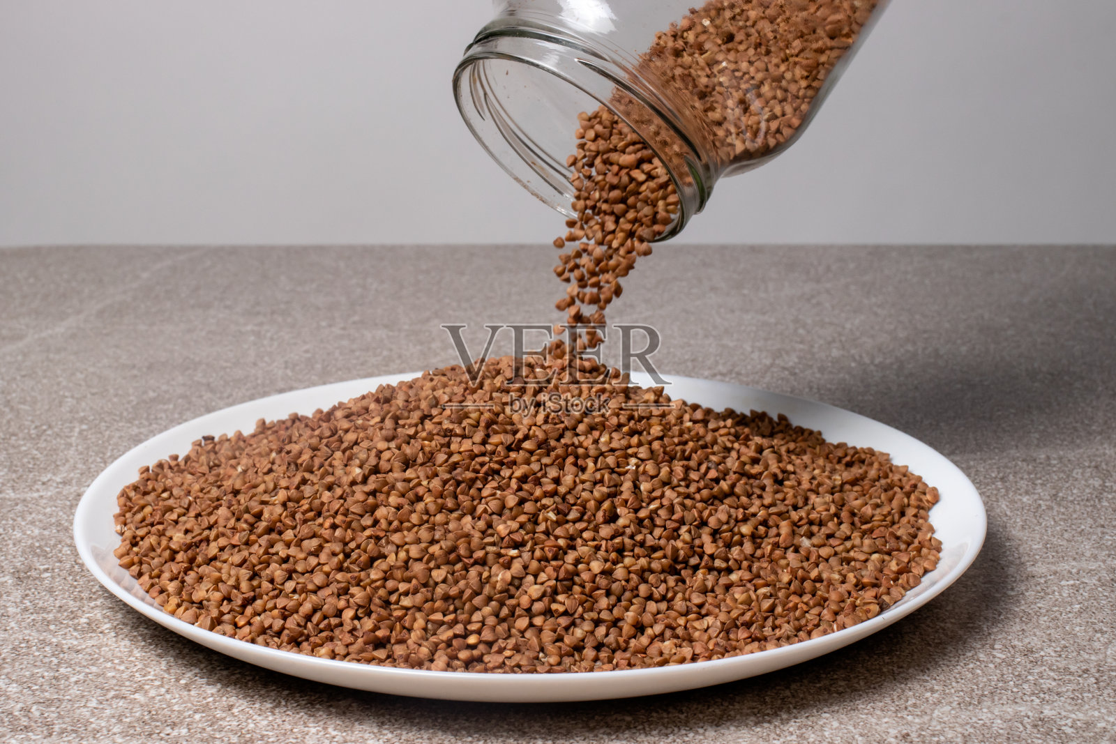 把荞麦从玻璃罐里倒进盘子里的过程。照片摄影图片