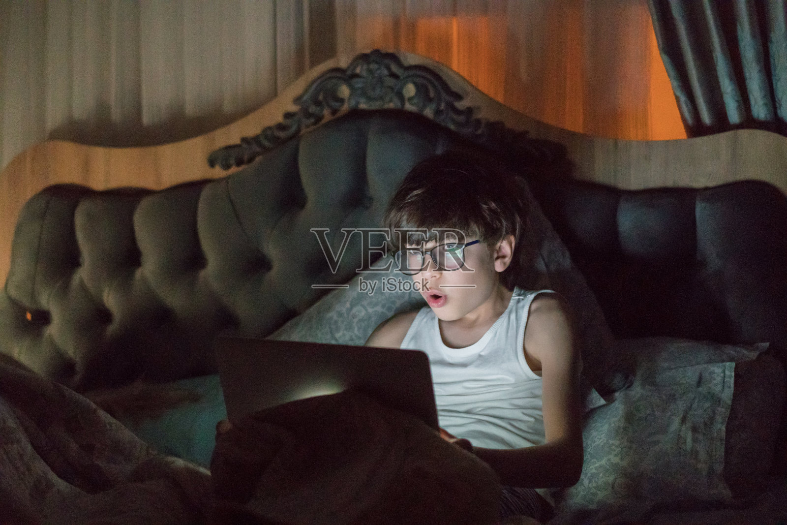 青少年男孩晚上在床上使用笔记本电脑照片摄影图片