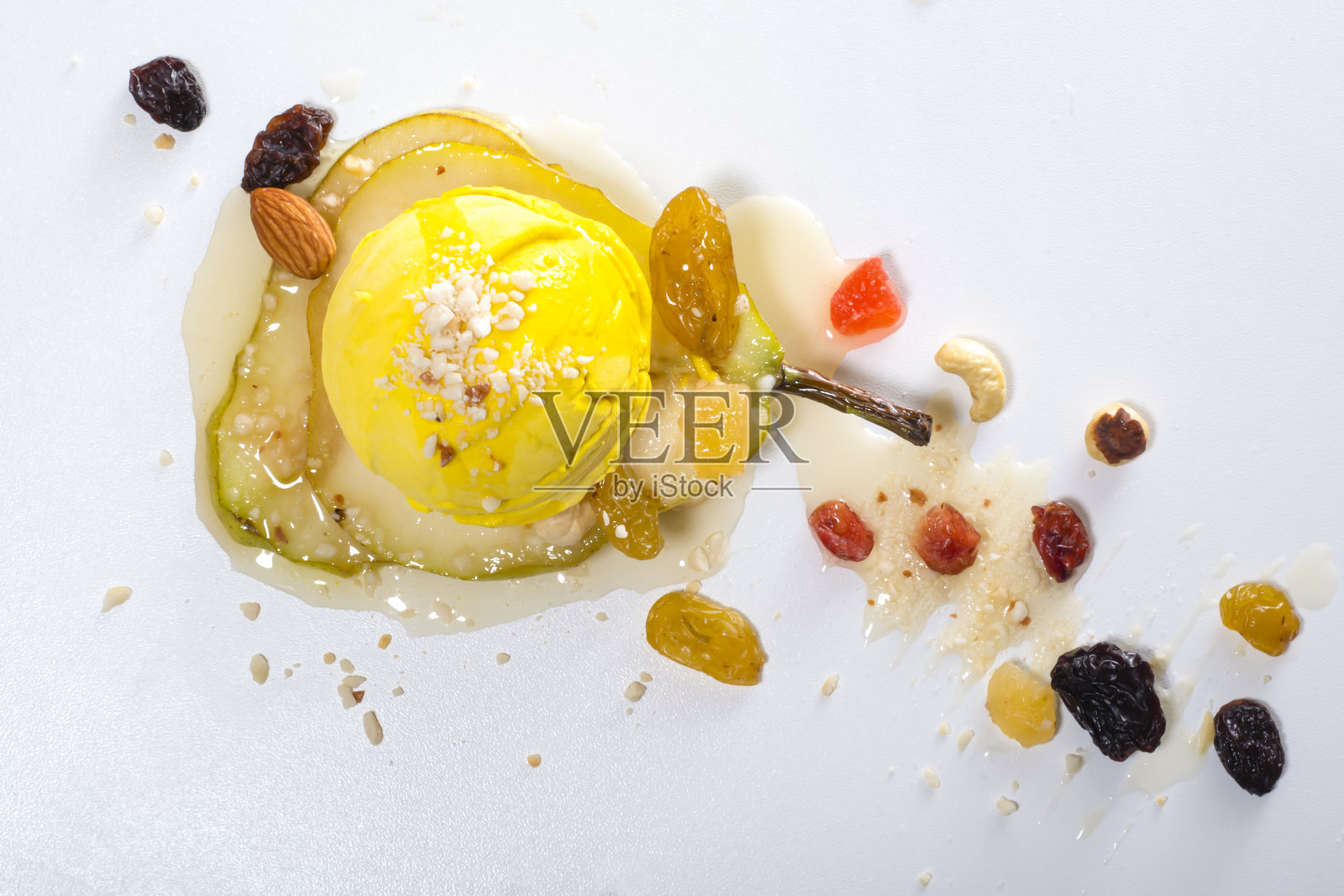 柠檬冰淇淋在一片梨子上，加上蜜饯水果和坚果，浇上糖浆在白色的表面上。照片摄影图片