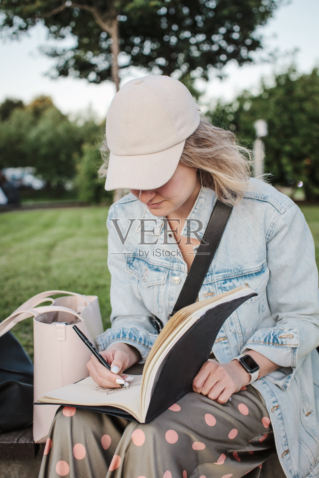 年轻漂亮的女孩在公园里画画。在速写本上写大纲。绘画课照片摄影图片