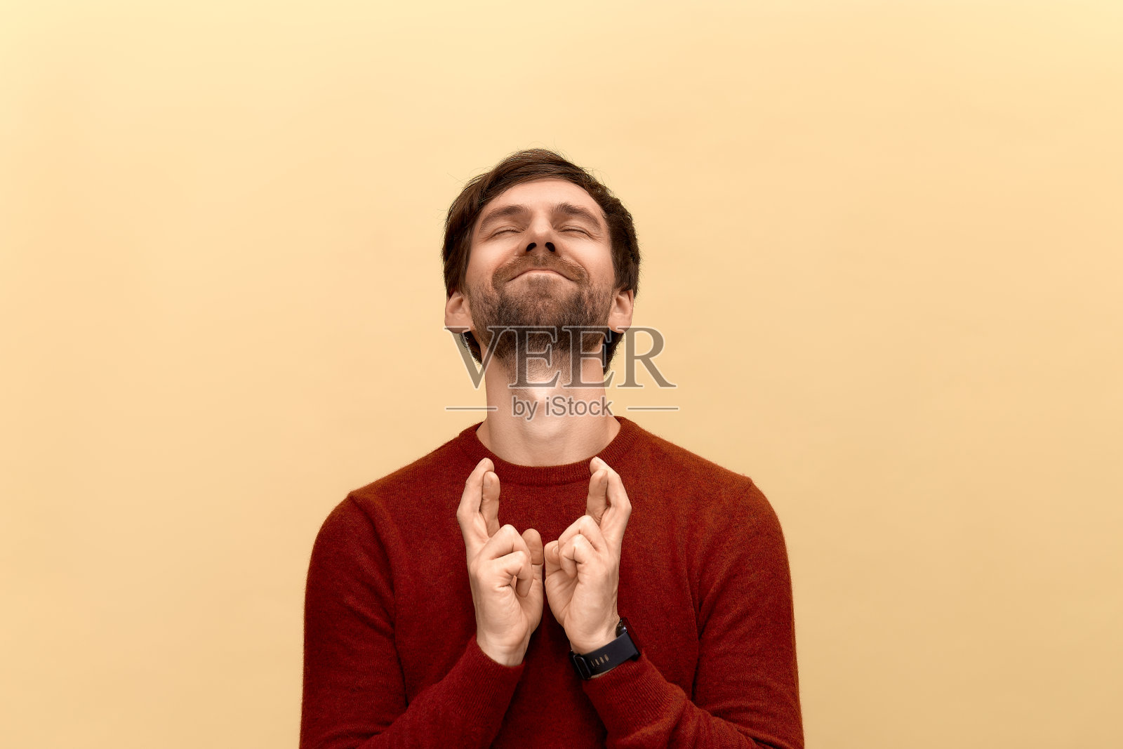 我一定要赢。年轻男子的照片与胡子穿毛衣，抬头，举起手指交叉，使理想的愿望，在黄色的背景摆姿势。照片摄影图片