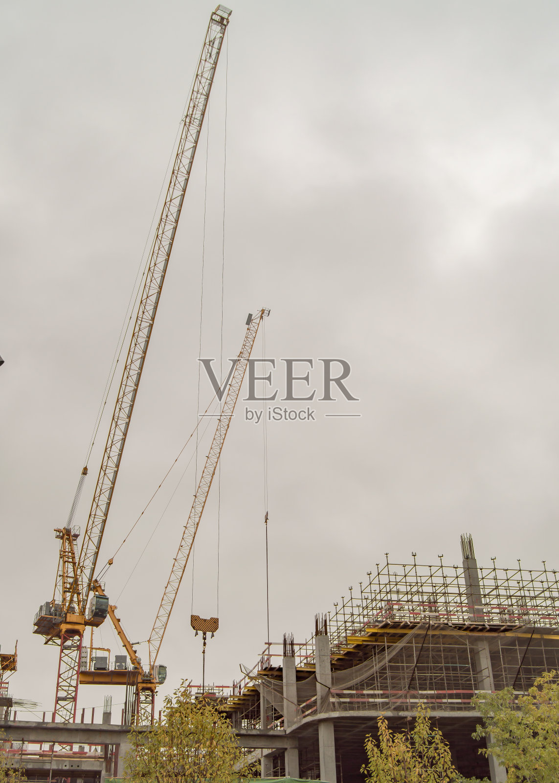 一座建筑起重机和一座由混凝土桩和铁制成的建筑，一个建筑工地映衬着阴沉沉的灰色天空，垂直照片摄影图片
