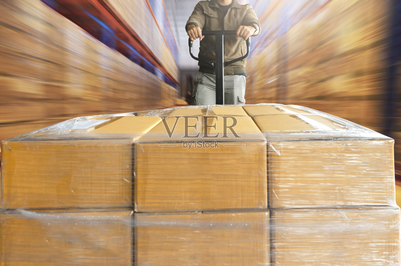 运动模糊的工人工作与手动托盘卡车，他是卸货箱在大型仓库存储。照片摄影图片