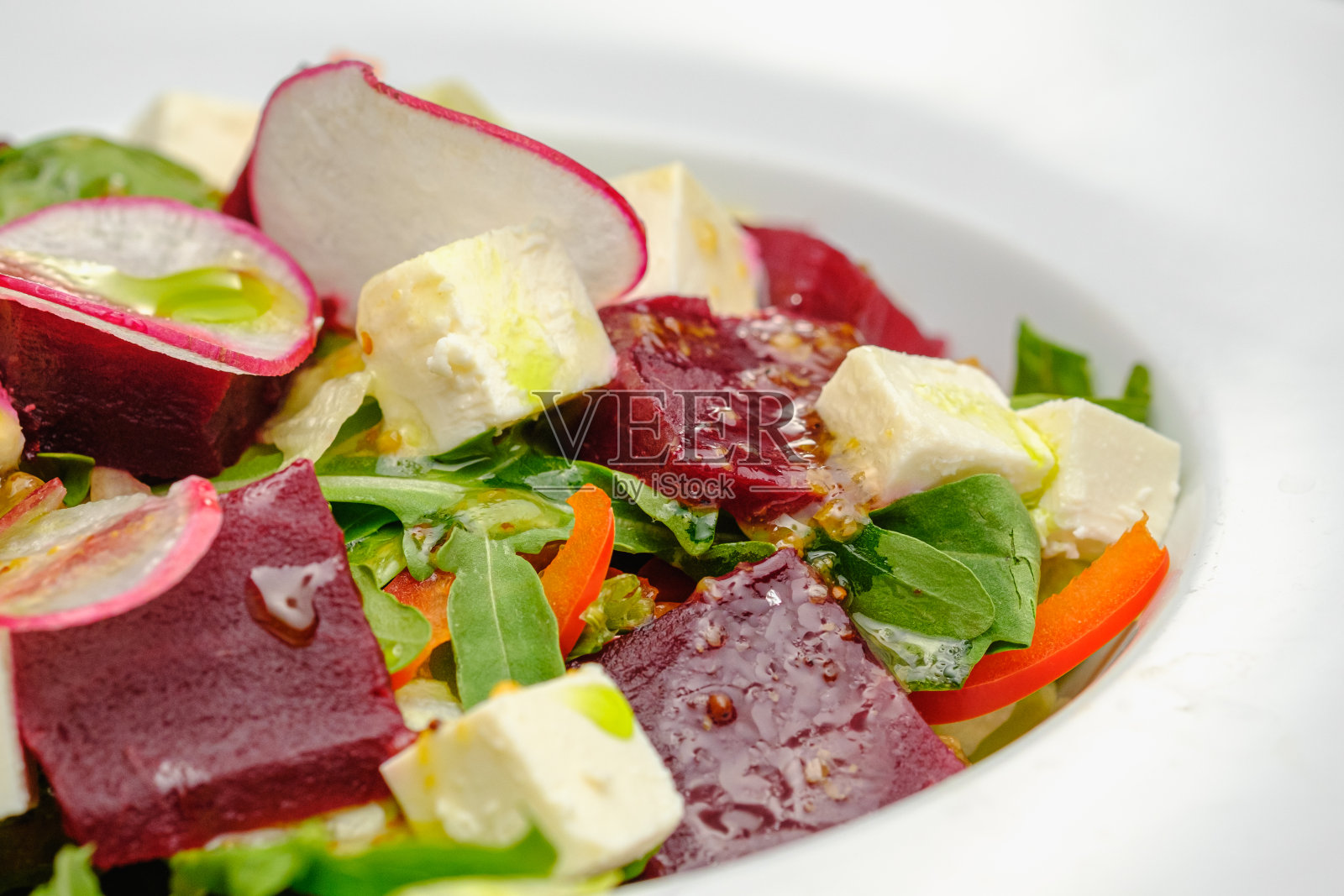 蔬菜沙拉，白盘，灰色背景，白萝卜，软奶酪，甜菜根和绿色蔬菜。餐厅里的零食。照片摄影图片
