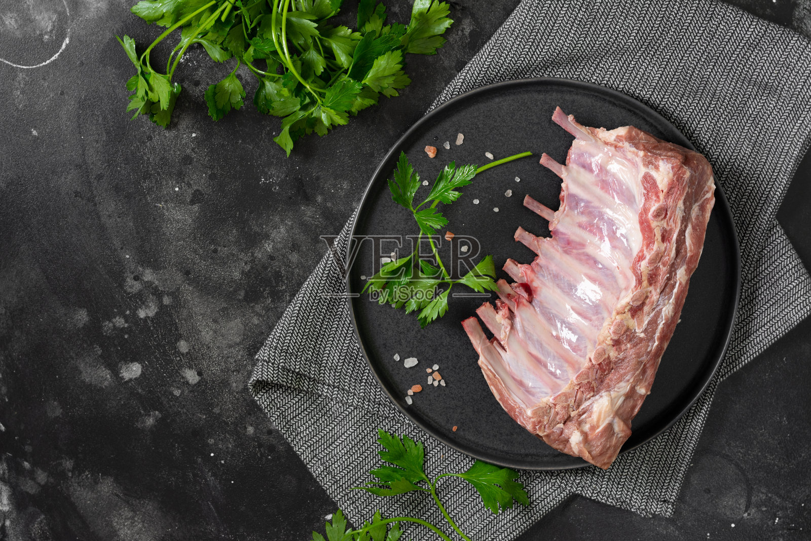 小羊羔的生排骨。黑色餐桌上的黑色陶瓷盘子里的生羊排骨。桌上的小羊羔的生肉照片摄影图片