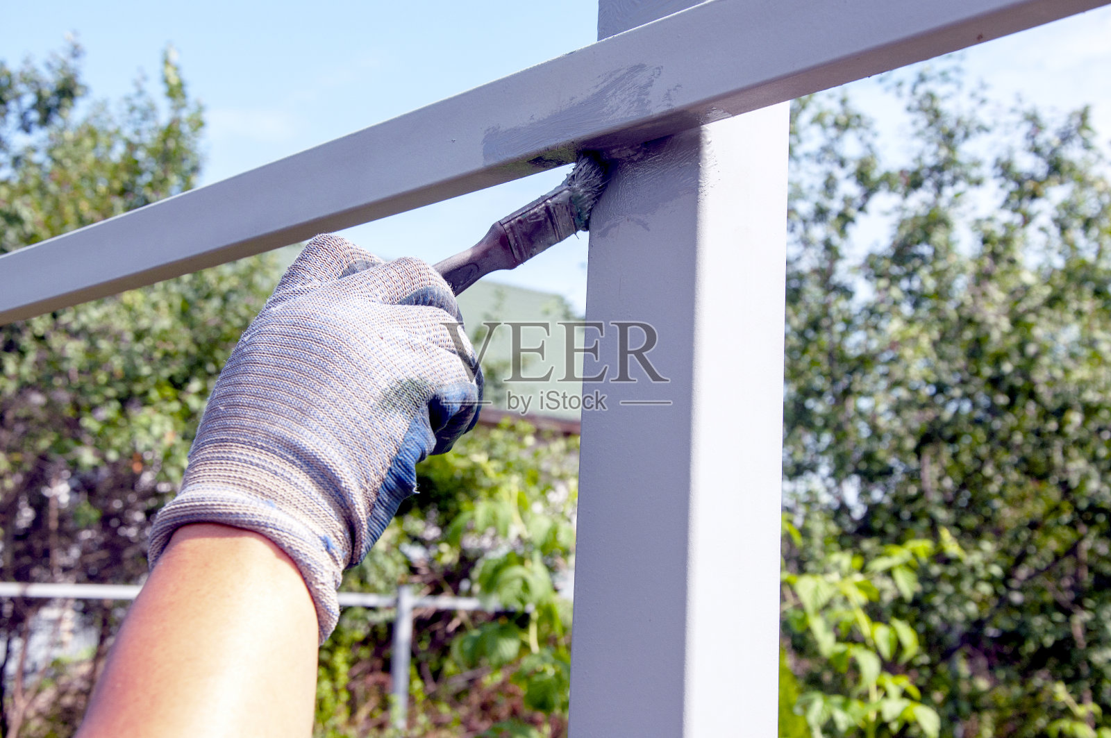 油漆生锈剥落的栅栏棒的过程。男人用篱笆刷着刷子。关闭宏。照片摄影图片