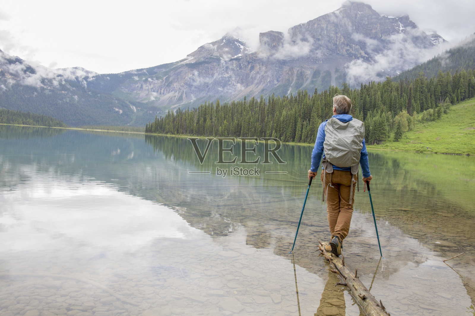 徒步旅行者沿着漂浮在高山湖上的圆木平衡照片摄影图片