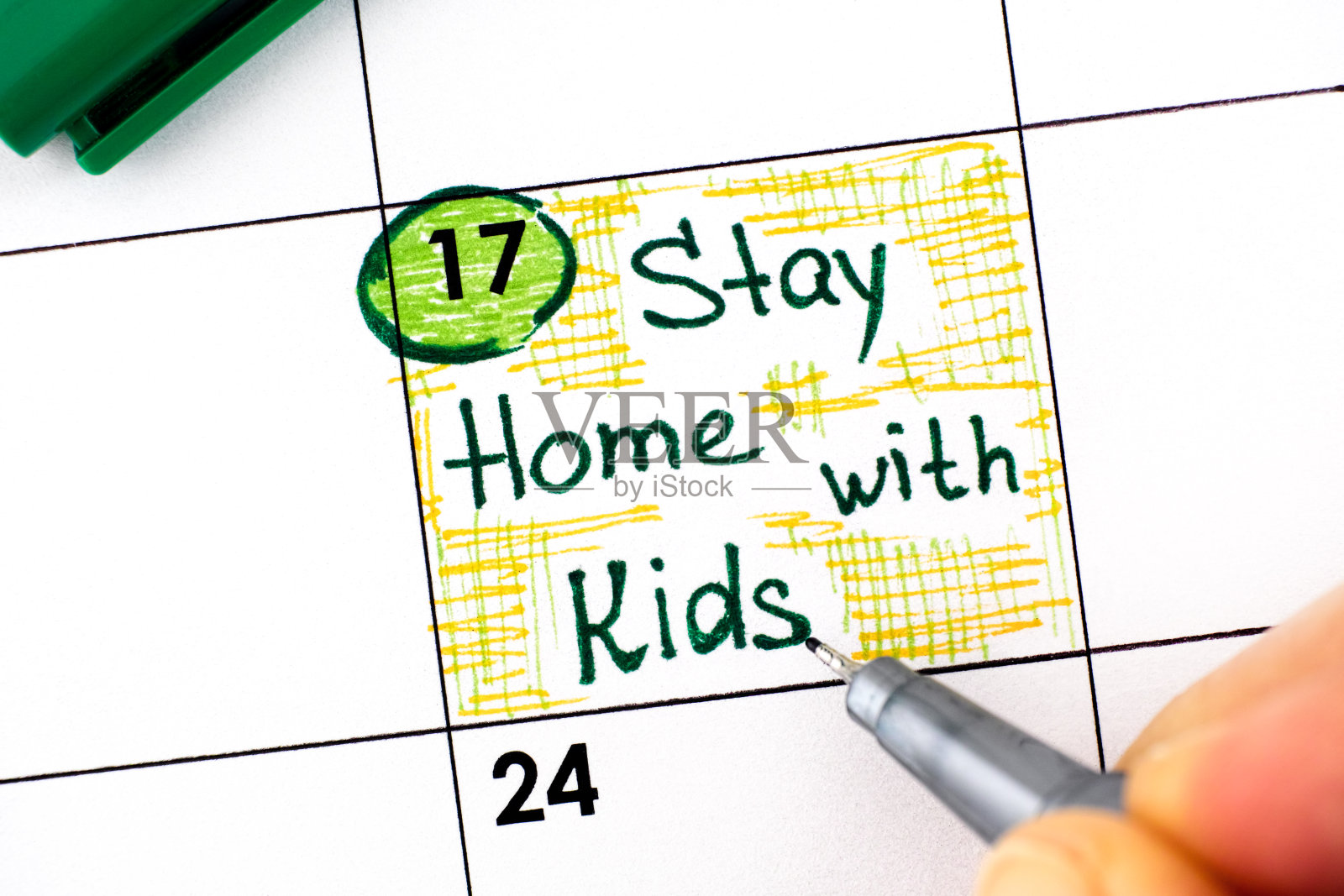 女人用手指用笔在日历上写下“待在家里陪孩子”的提醒。8月17日。照片摄影图片