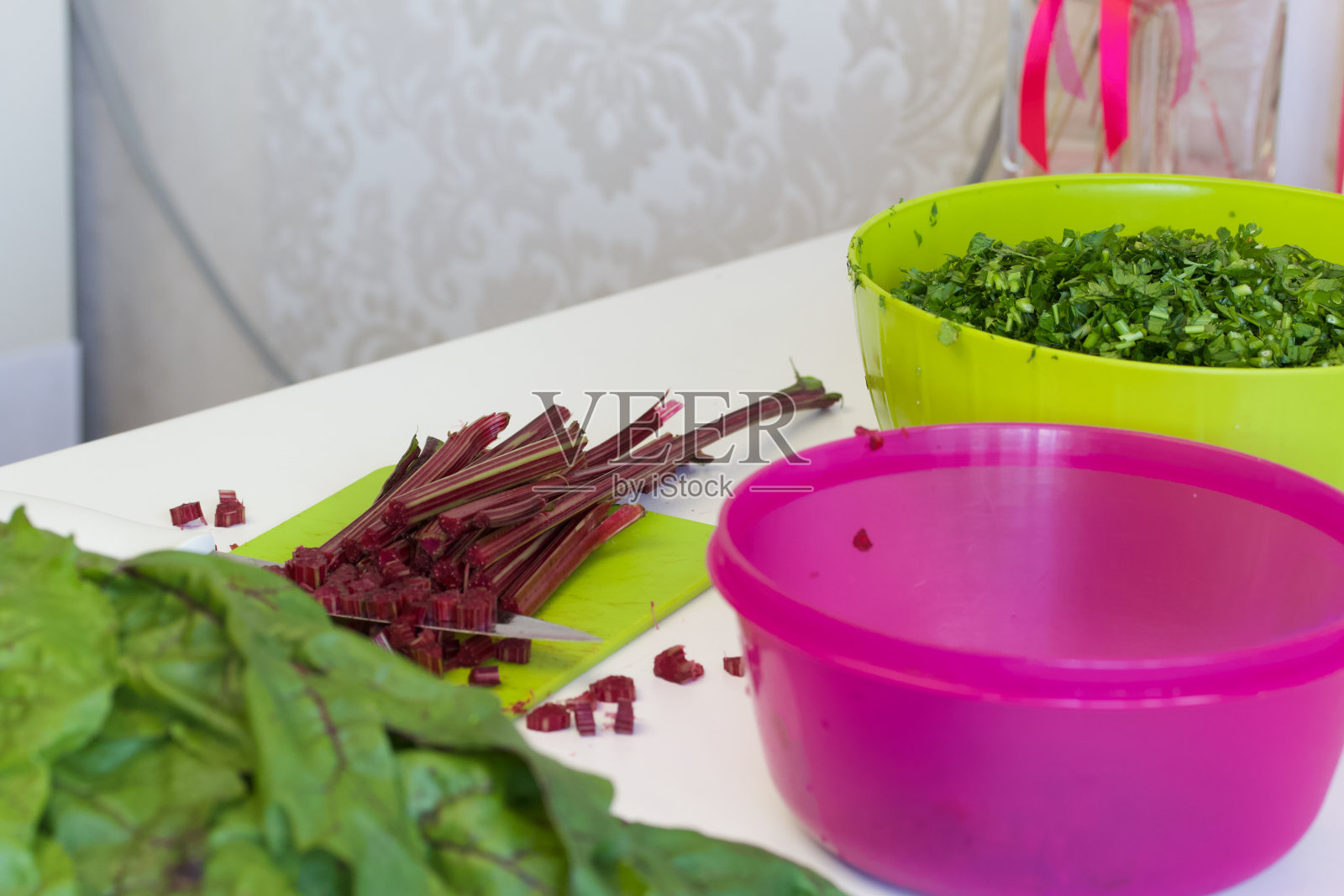 为冬天收割绿色植物。在桌面上放一些欧芹和甜菜。切菜板和刀。容器里是碎欧芹。照片摄影图片