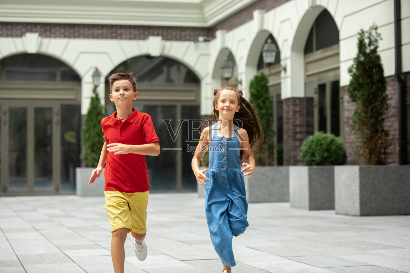 两个微笑的孩子，男孩和女孩一起跑在城里，在夏天的一天照片摄影图片