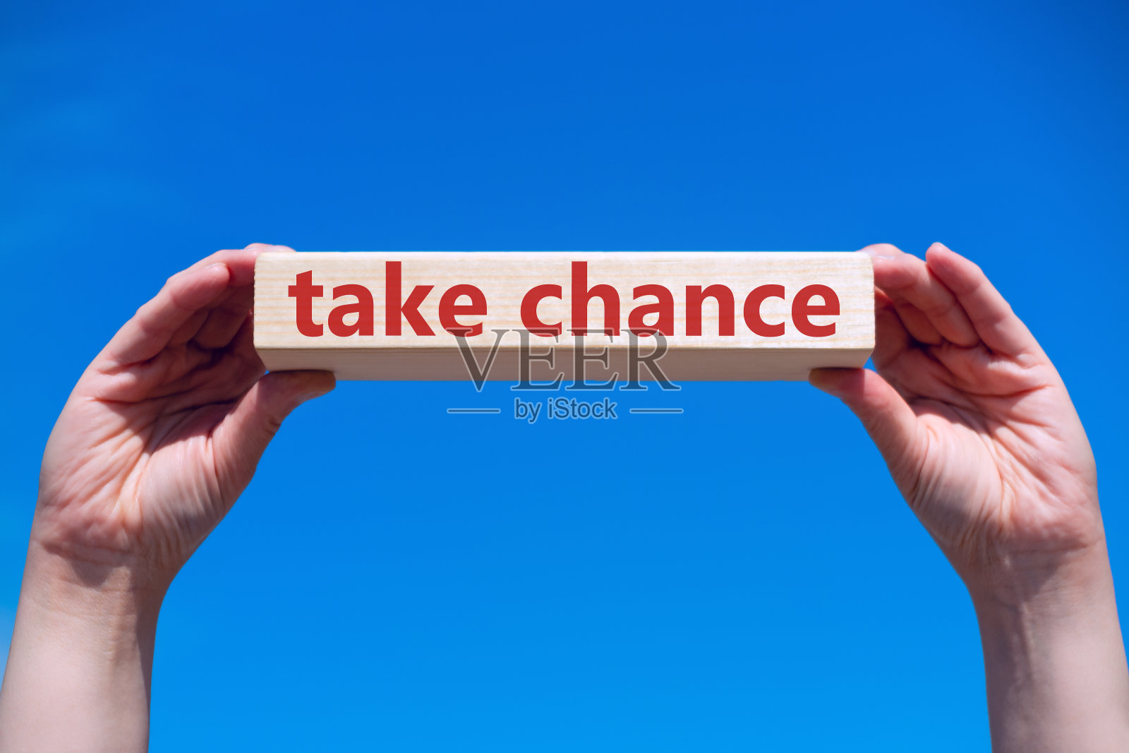 在蓝天的映衬下，人手握着一块写着“TAKE CHANCE on”的木块。成功和积极的思想观念。照片摄影图片