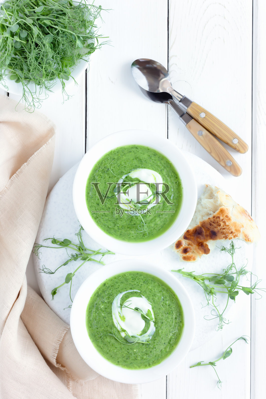 花椰菜和菠菜奶油汤，与面包和微型绿色蔬菜在一个白色的碗在一个木制的桌子。照片摄影图片