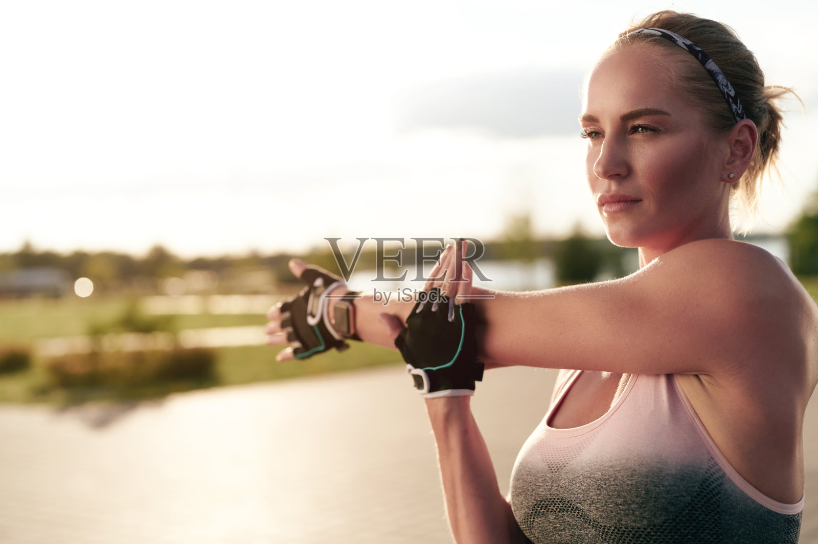 运动强壮的女人伸展手臂后跑。健身女性在城市建筑附近户外做热身运动照片摄影图片