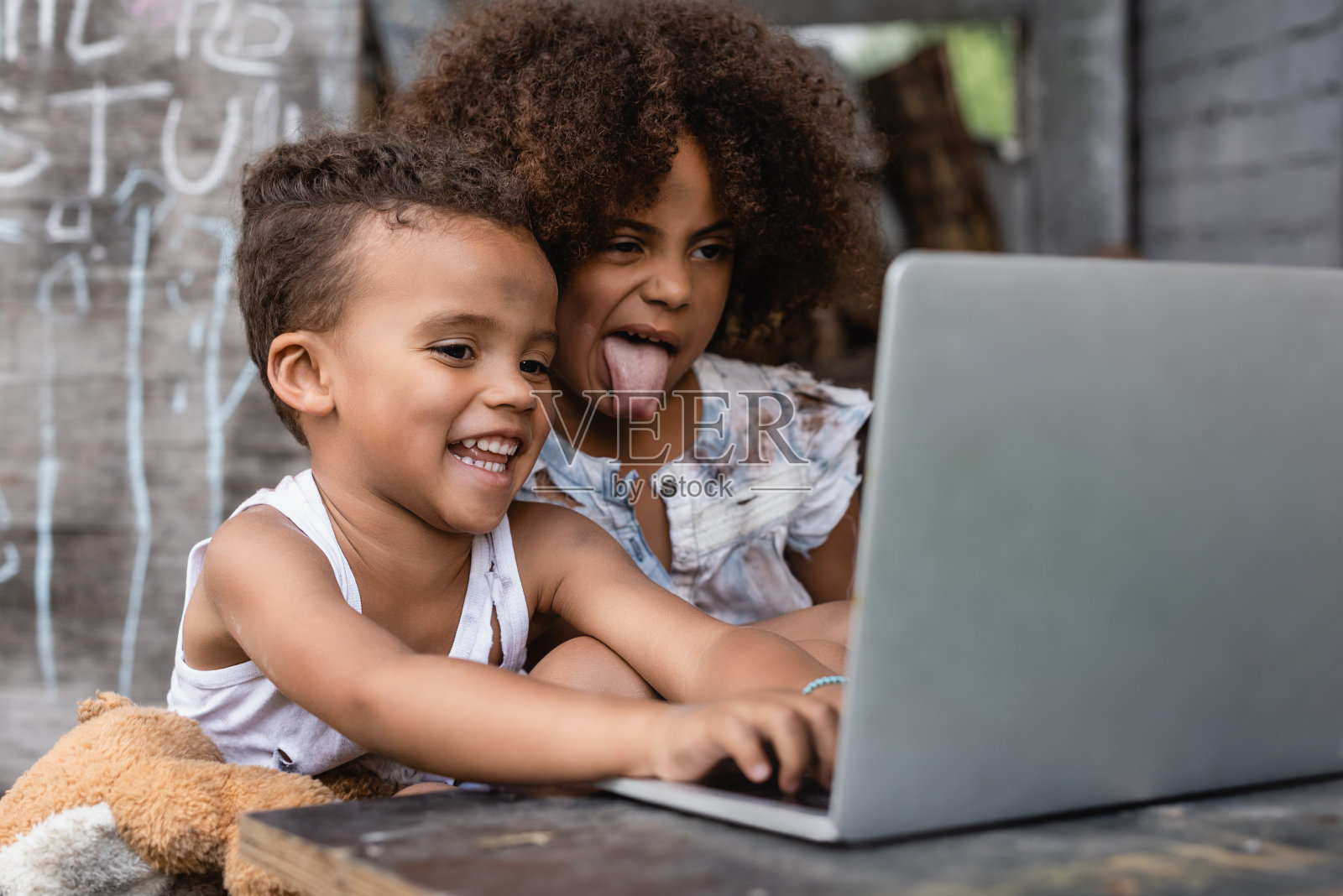 可怜的非洲裔美国孩子在快乐的孩子旁边伸出舌头，在外面用笔记本电脑照片摄影图片