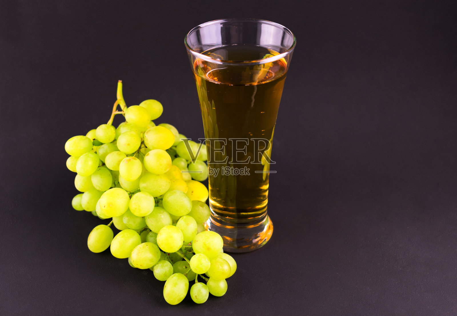 一个在黑色背景上有葡萄汁和一串葡萄的玻璃杯。照片摄影图片