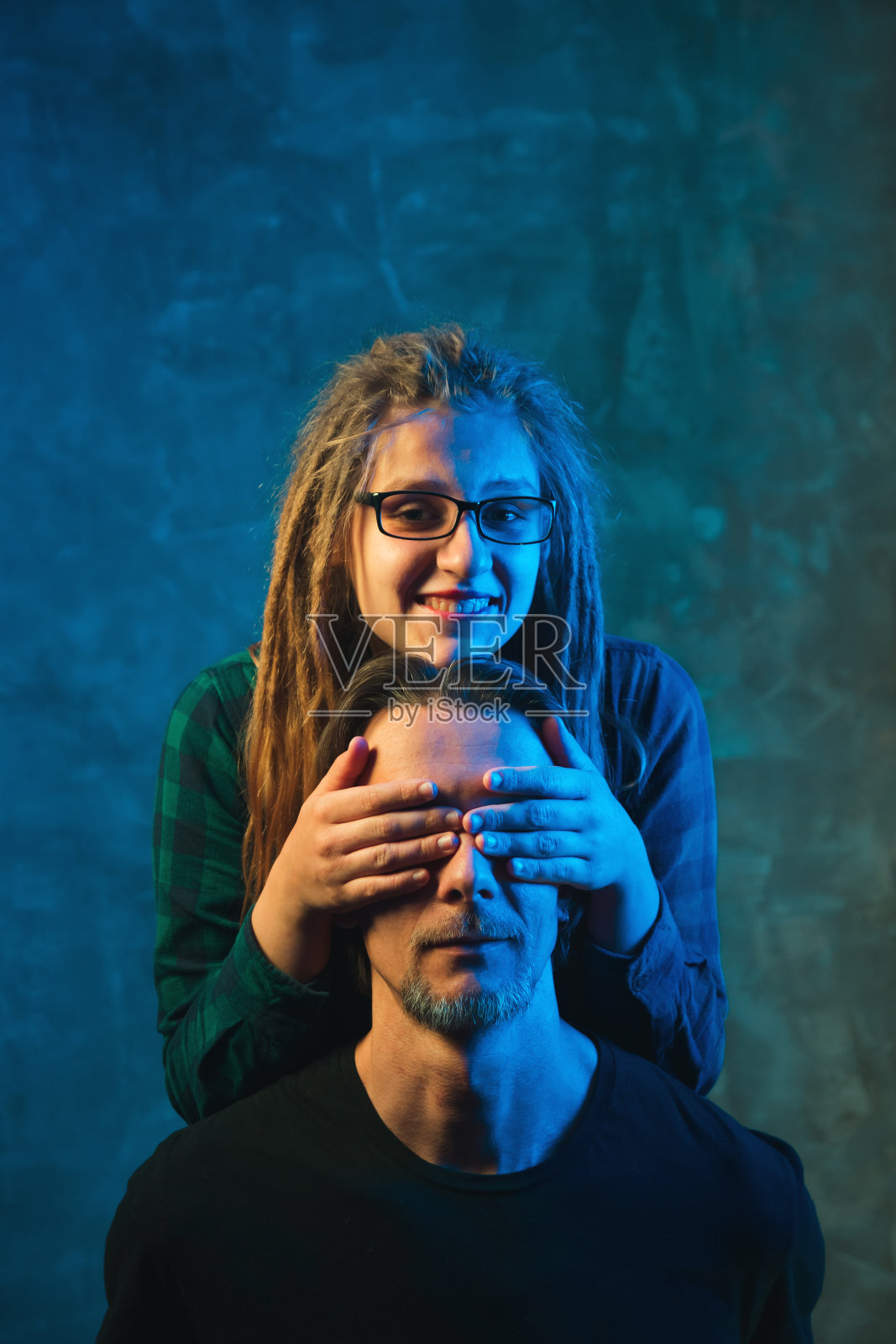 一名男子和一名年轻女子在彩色灯光下，在黑暗的背景下摆姿势。照片摄影图片