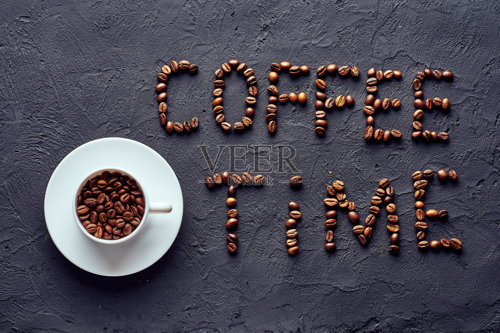 在白色瓷杯上的托盘上放置烤好的整颗咖啡豆，灰色背景上刻有咖啡豆的咖啡时间照片摄影图片