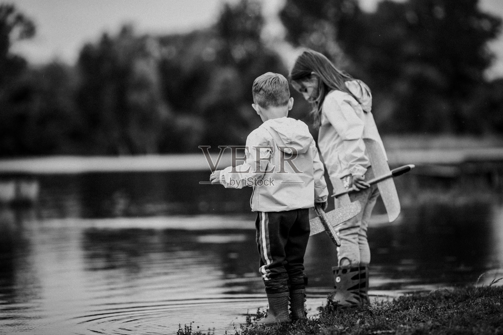 一个孩子站在河边，手里拿着玩具的黑白图像照片摄影图片