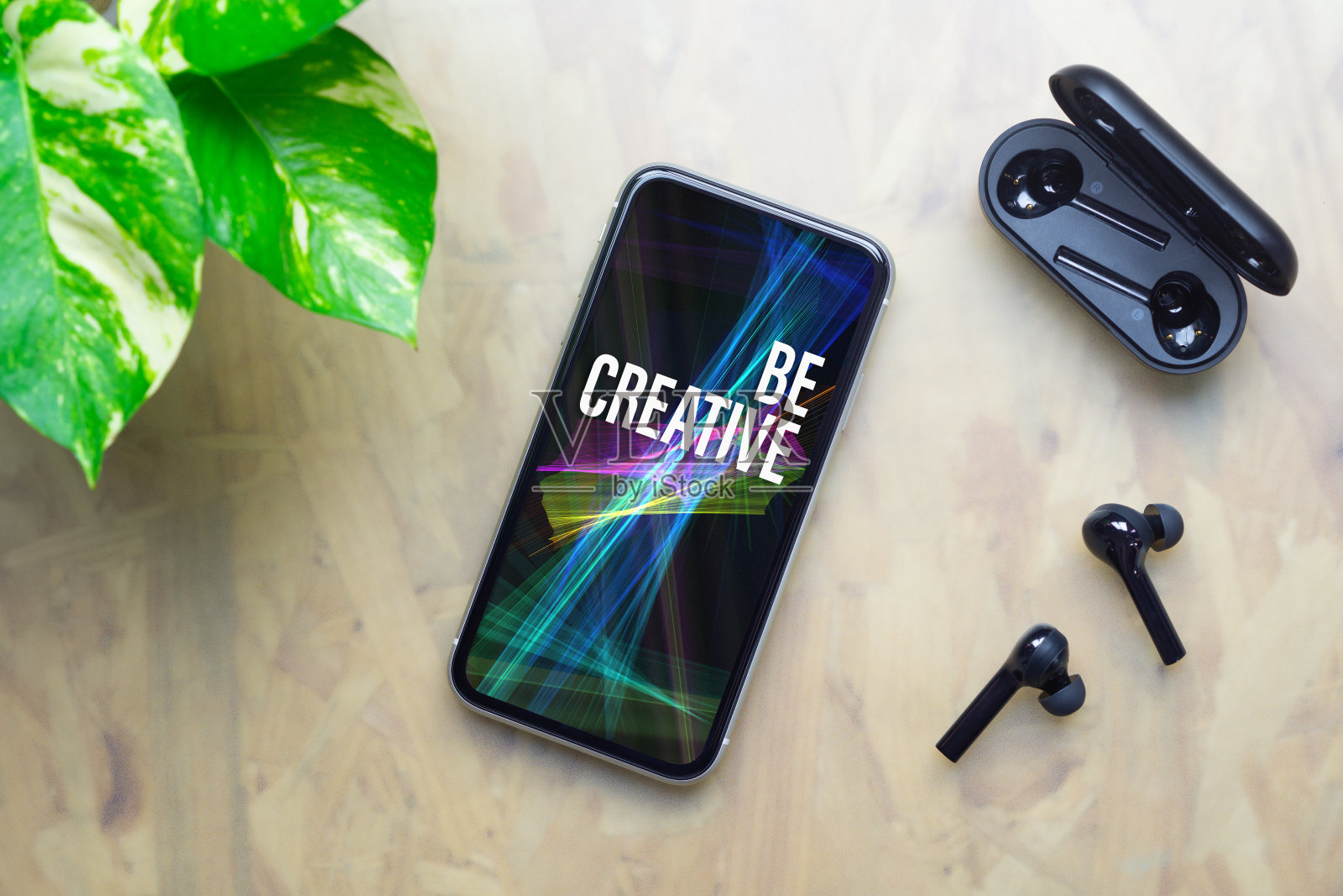是创意灵感的背景概念。平躺俯视图的创意文本智能手机与无线耳机和充电盒在工作办公桌上。照片摄影图片