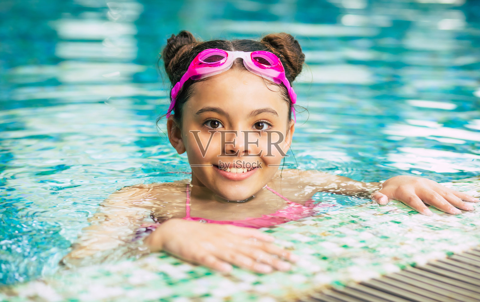 快乐美丽的小女孩微笑在护目镜和泳衣在游泳池有乐趣，而度假或游泳课。照片摄影图片