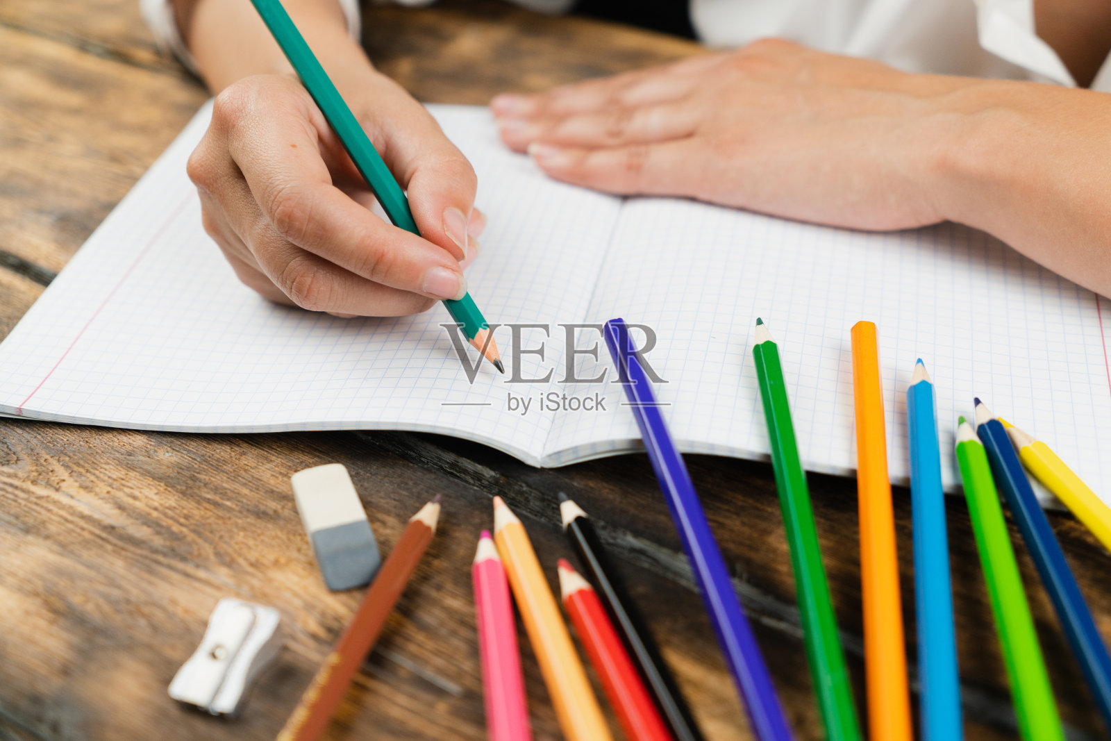 这个女学生坐在课桌前，用彩色铅笔在笔记本上画画。照片摄影图片