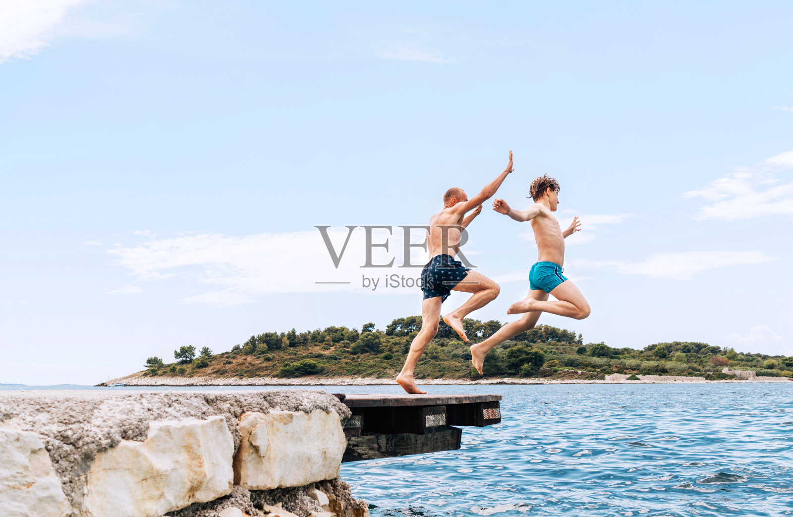 父亲和儿子在亚得里亚海海岸度过了一个快乐的假期。他们从码头跳到岸边穿上泳裤。家庭时间，童年或父亲的概念形象。照片摄影图片