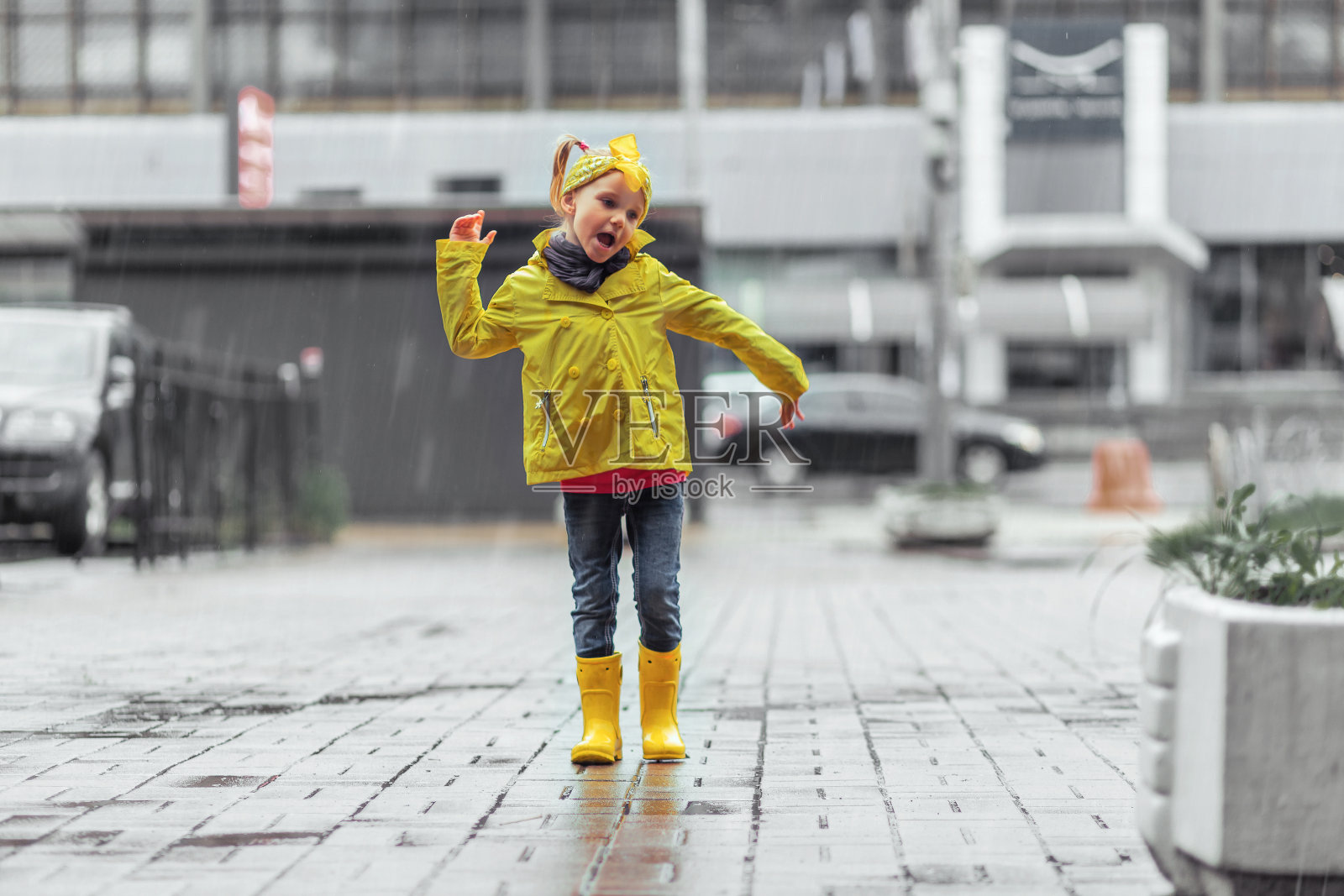 秋日里穿着黄色雨衣和雨靴在停车场水坑里玩耍的女孩照片摄影图片