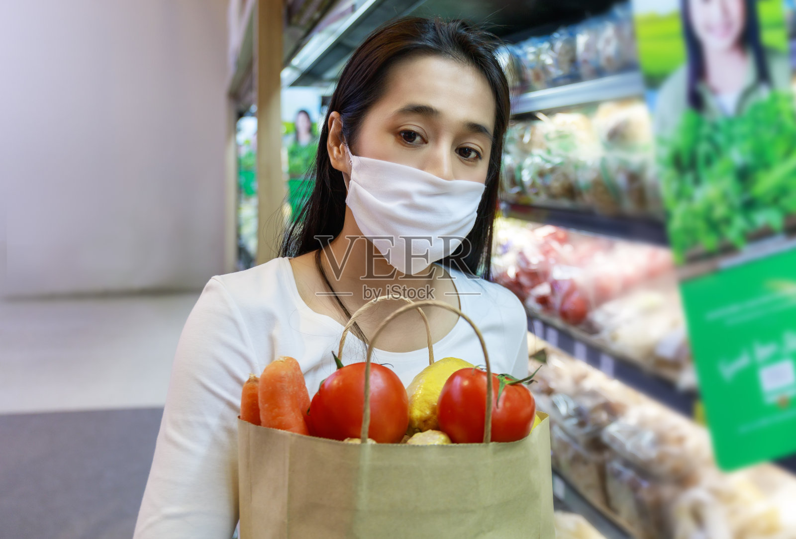 亚洲妇女戴着保护面罩，拿着装着水果和蔬菜的纸袋在超市购物。女孩，去杂货店买水果。新冠肺炎疫情后的新常态。家庭的概念。照片摄影图片