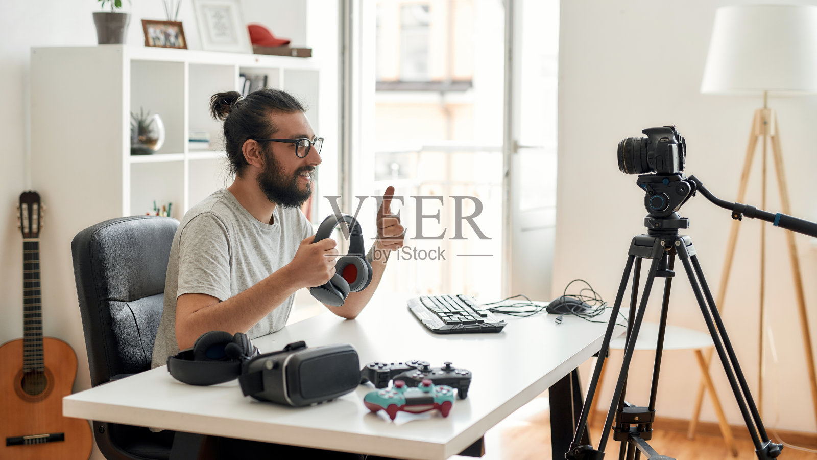 男性科技博主拿着耳机，竖起大拇指在家庭工作室录制关于新设备的视频博客或视频博客照片摄影图片