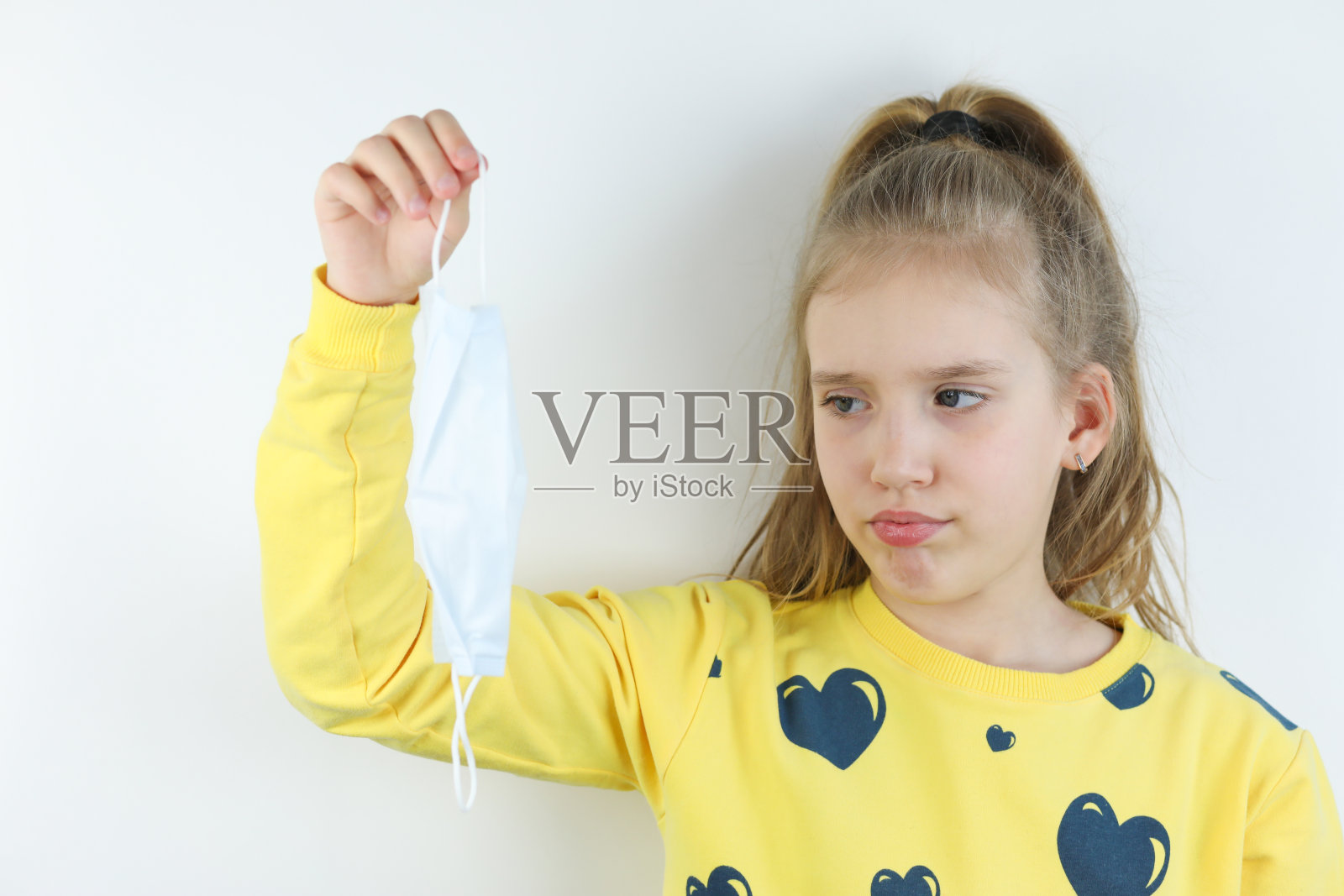 美丽的女孩，白色背景上黄色t恤的孩子脱下医疗保健防护面具。标志着冠状病毒大流行、大流行、爆发或隔离的结束照片摄影图片