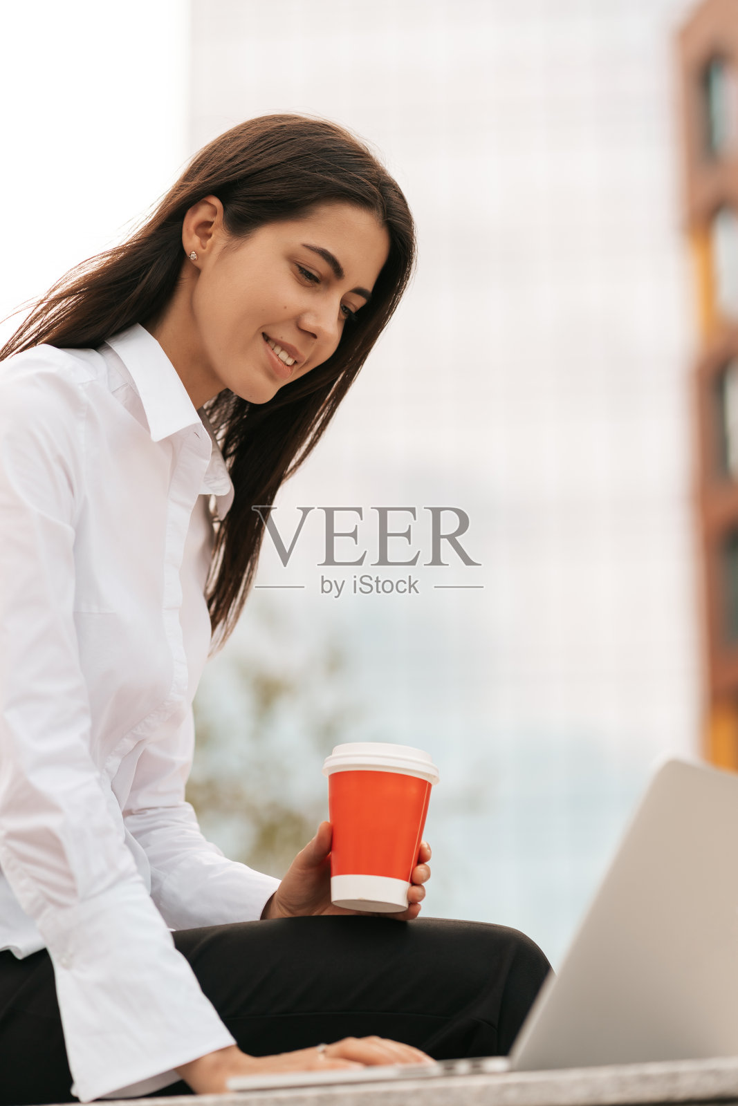 美丽的女人微笑着使用笔记本电脑，而坐和工作照片摄影图片